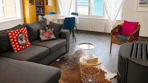 A living room with a sofa, a dining table, a bookshelf, and a view of the sea.
