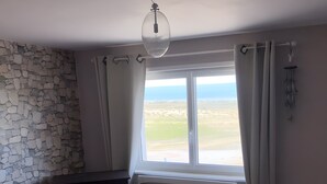 A bedroom with a stone wall, a bed, a window with curtains, and a ceiling light.