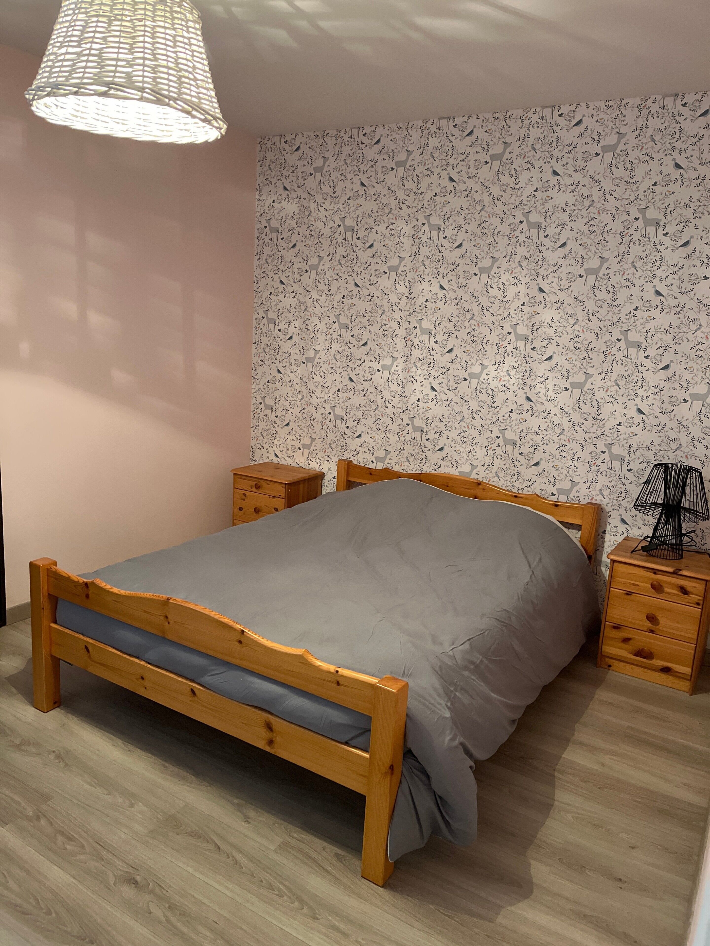 A bedroom with a wooden bed, two nightstands, a patterned wallpaper, and a hanging light fixture.