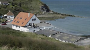 A coastal house with a sloped roof, a satellite dish, and a view of the sea.