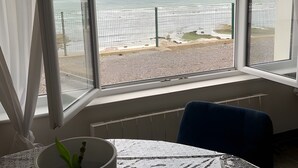 A room with a large window overlooking a beach, a table with a white tablecloth, and a chair.