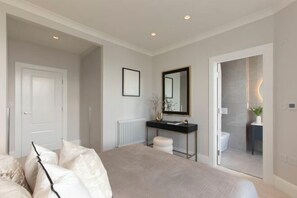 A bedroom with a bed, a bedside table, a mirror, and a door leading to a bathroom. - 313 Premium Maisonette (London)