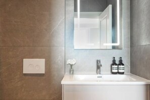 A modern bathroom with a white sink, a mirror with a light strip, and two bottles of hand soap. - 313 Premium Maisonette (London)