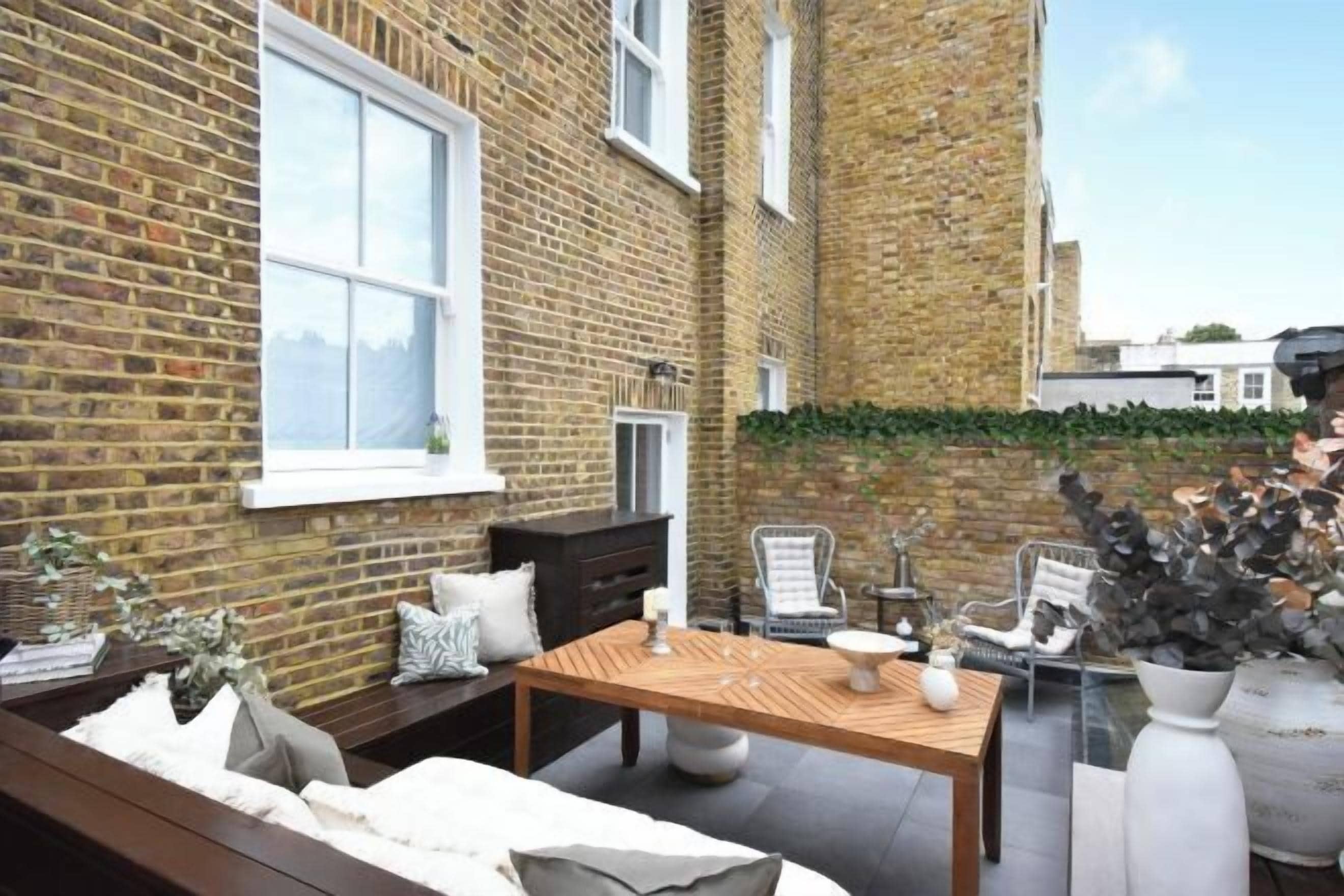 A brick courtyard with a wooden table and chairs, a bench, and a potted plant.