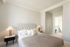 A bedroom with a tufted headboard, a large bed with a beige bedspread, two bedside lamps, and a view of a balcony through an open door. - 313 Premium Maisonette (London)