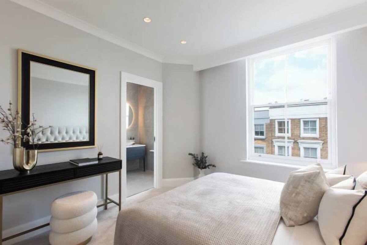 A modern bedroom with a large bed, a vanity with a mirror, and a view of the city through a large window.