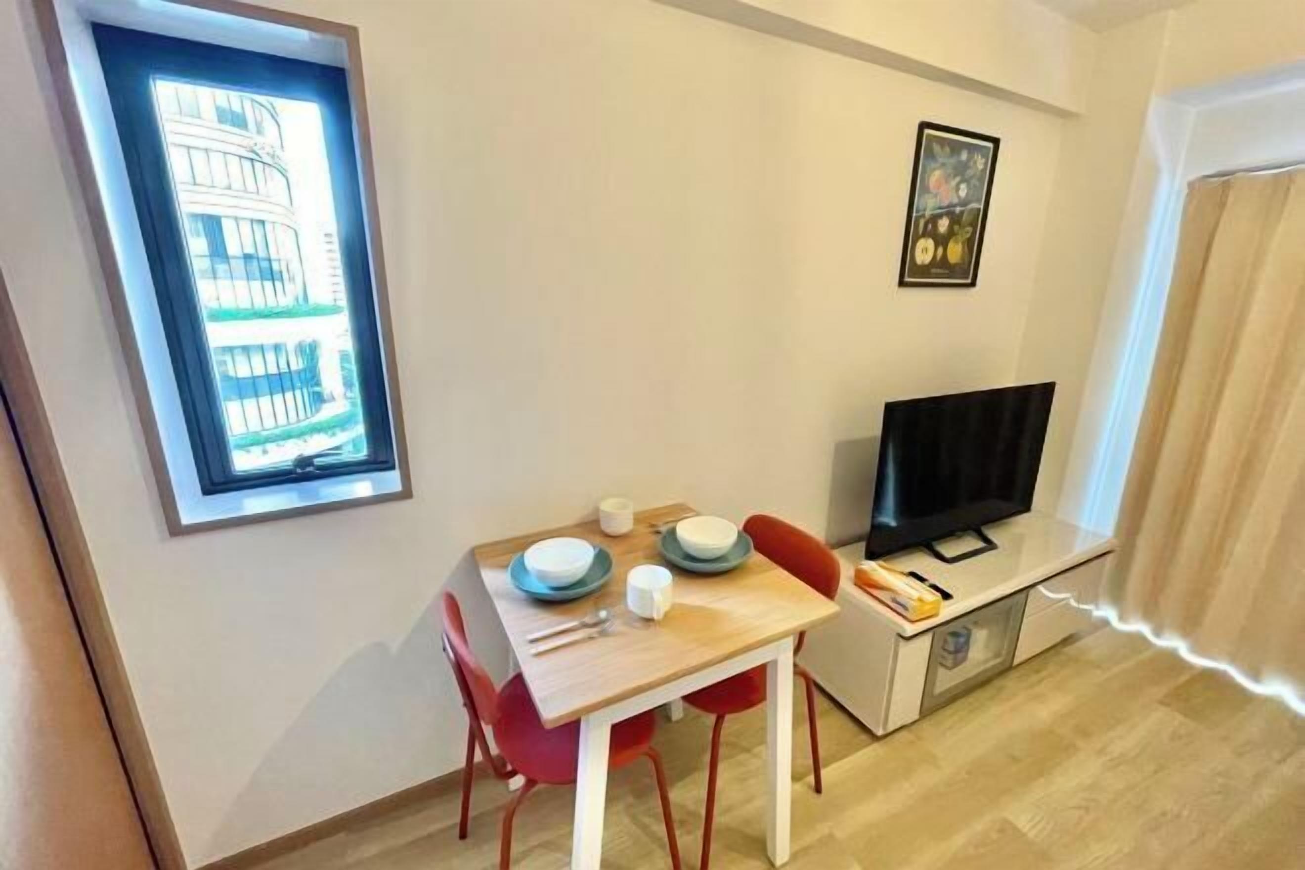 A small room with a dining table, chairs, a television, and a window with a view of a building. - YMK Oshiage 7B (Tokyo)