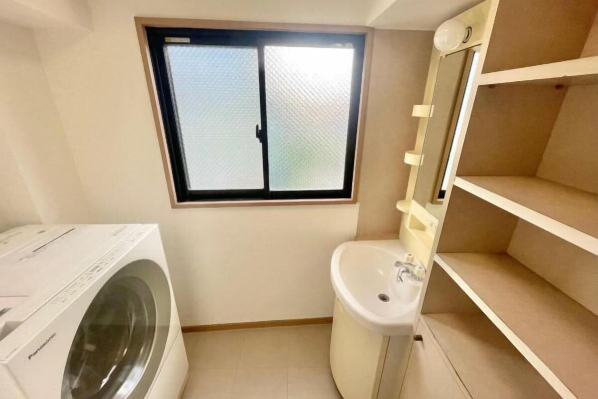 A compact bathroom with a washing machine, a toilet, and a window.