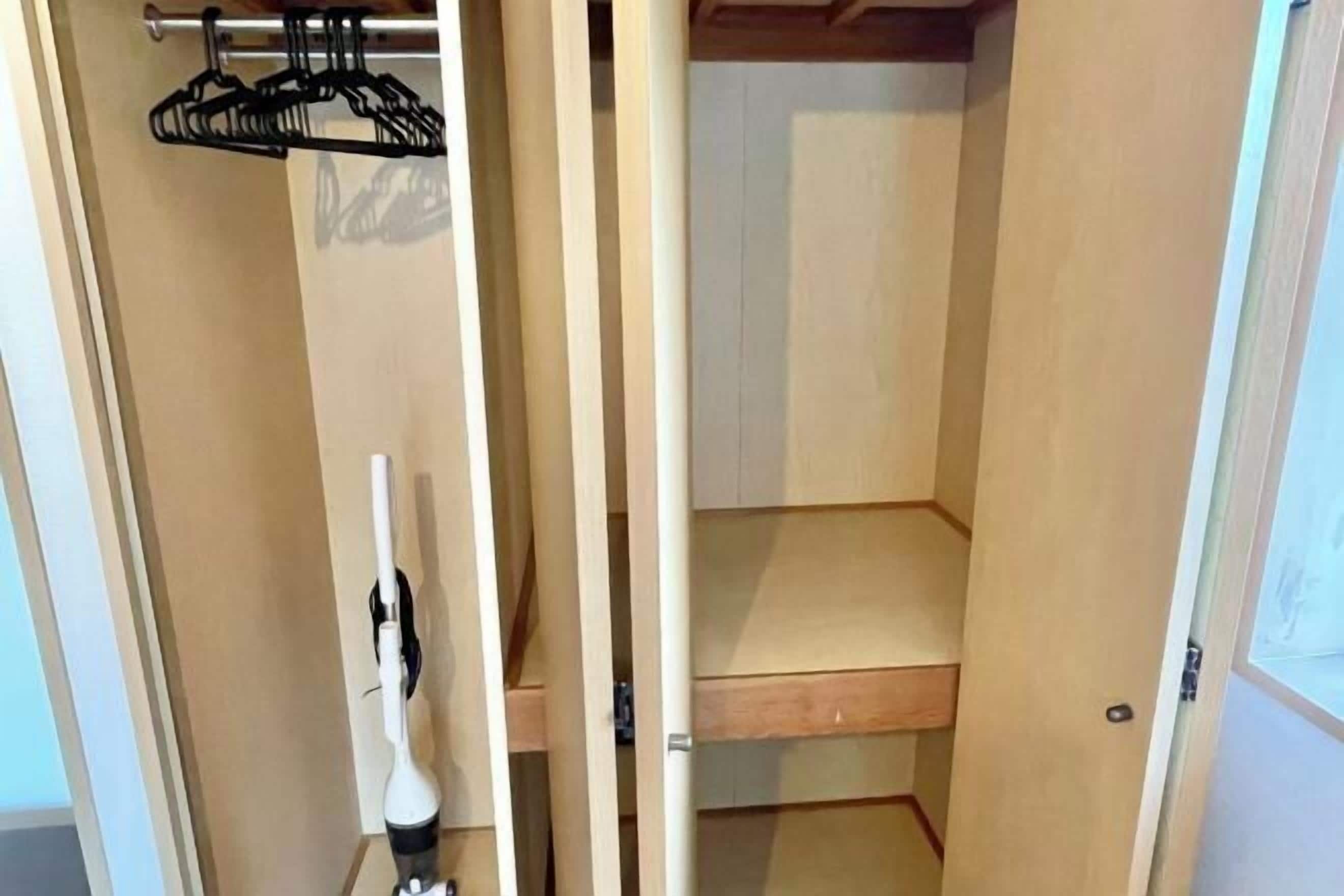 Un armario con puertas de madera, un perchero y una aspiradora.
