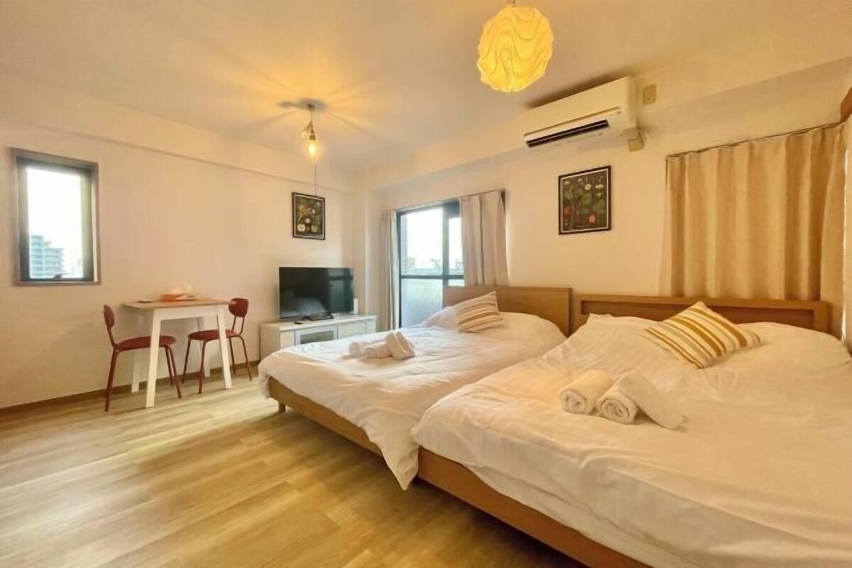 A hotel room with two beds, a desk, a chair, and a TV.