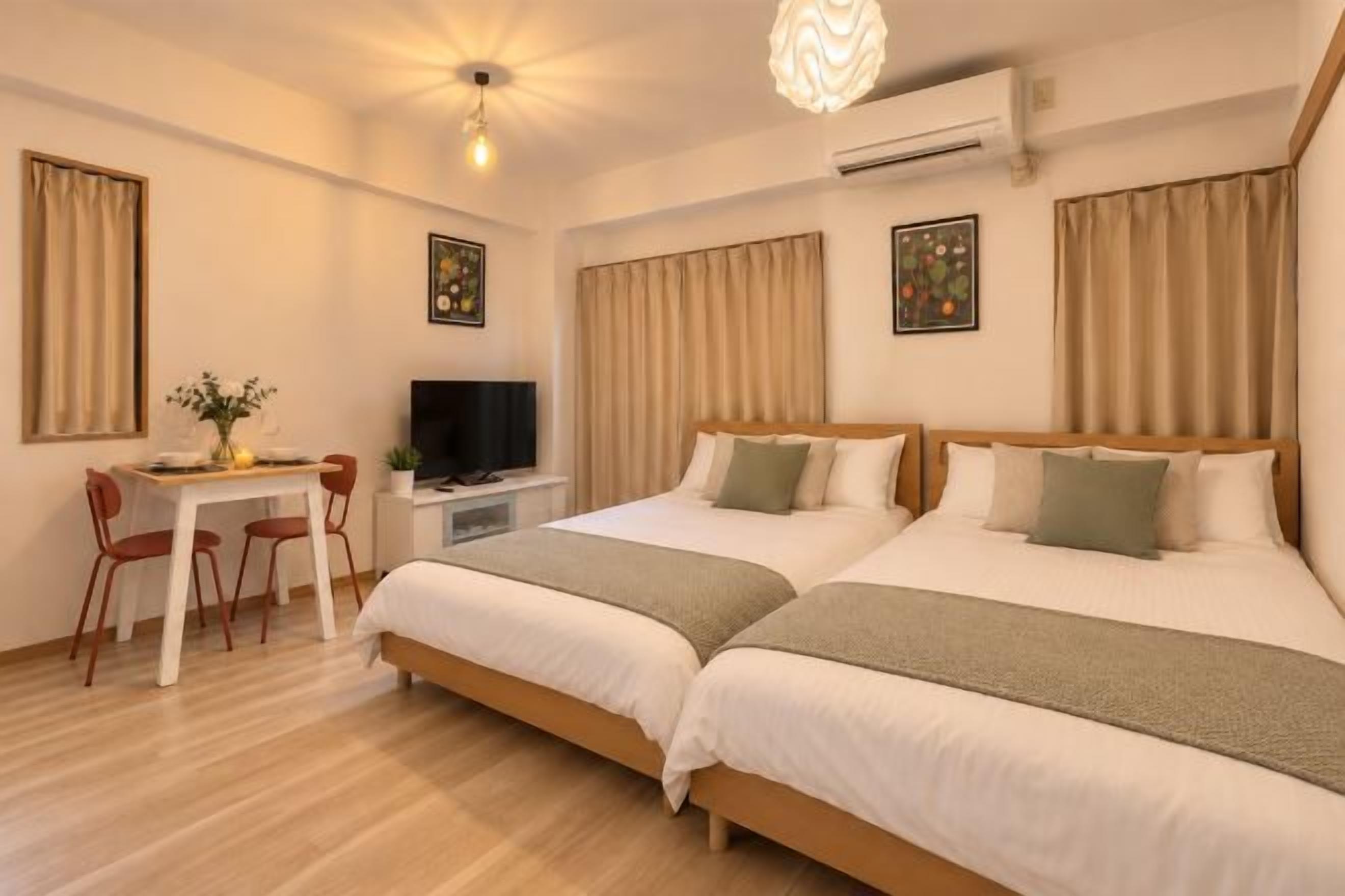 Quarto de hotel com duas camas, uma escrivaninha com cadeira, televisão e luminária no teto.