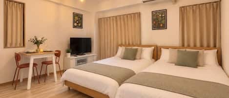 A hotel room with two beds, a desk with a chair, a television, and a ceiling light fixture.
