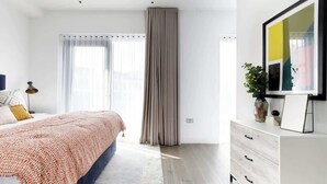 A modern bedroom with a large bed, a white dresser, and a framed picture on the wall.