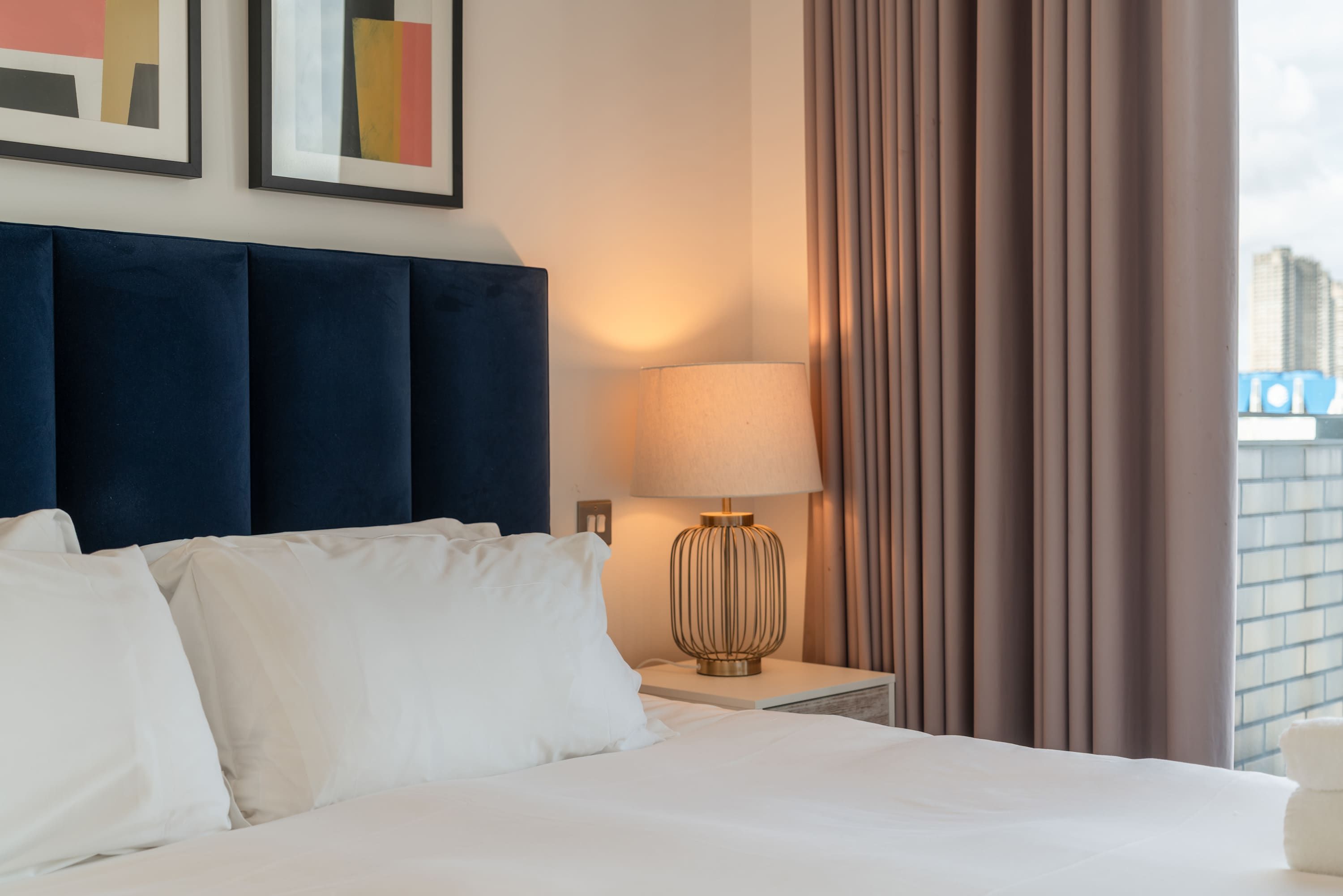 Een hotelkamer met een groot bed, een nachtkastje met een lamp, en uitzicht op de stad door het raam.