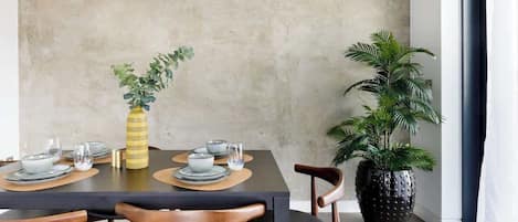 A dining area with a table set for four, chairs, a potted plant, and a textured wall.