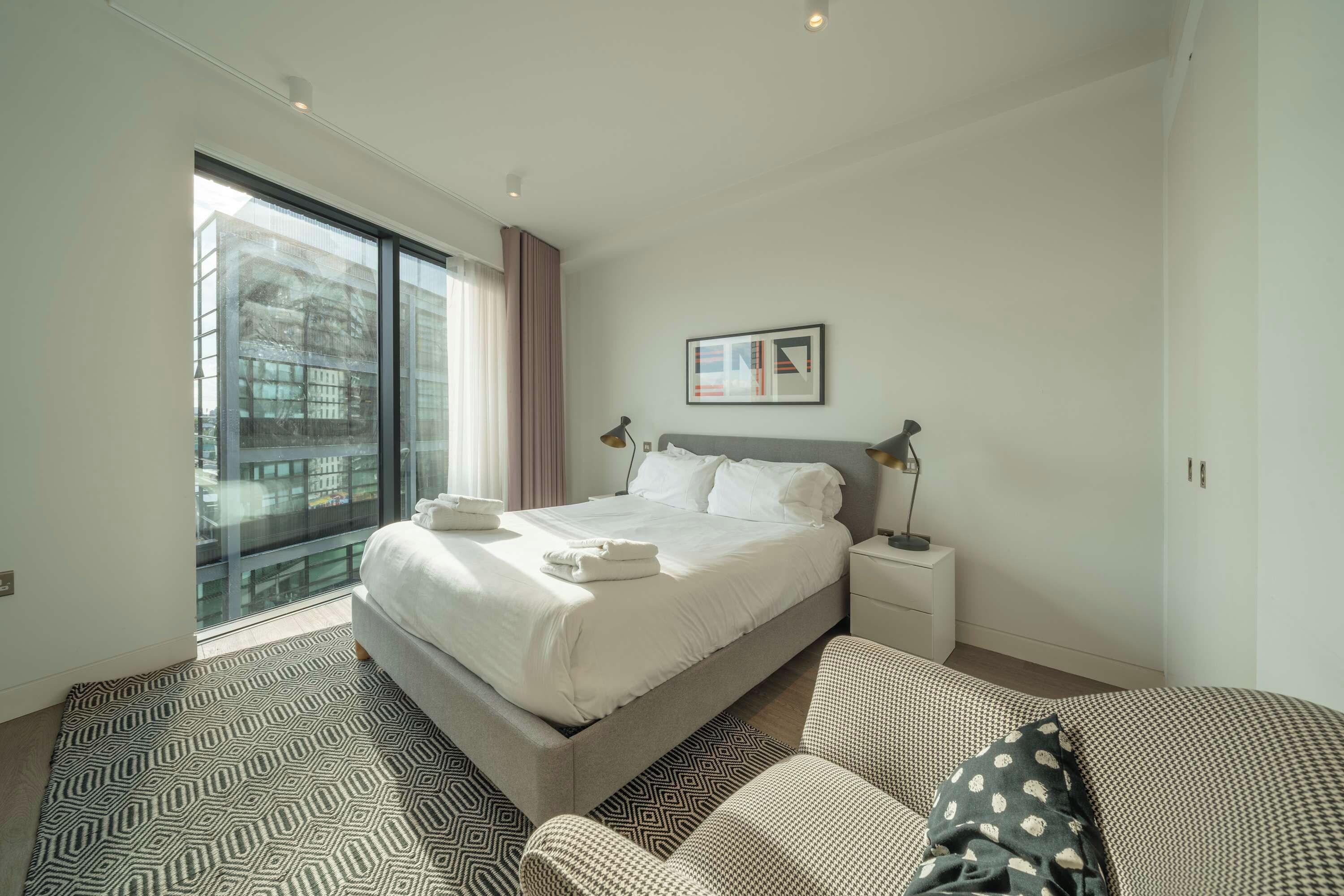 A modern hotel room with a large bed, bedside tables, a window with curtains, and a city view.