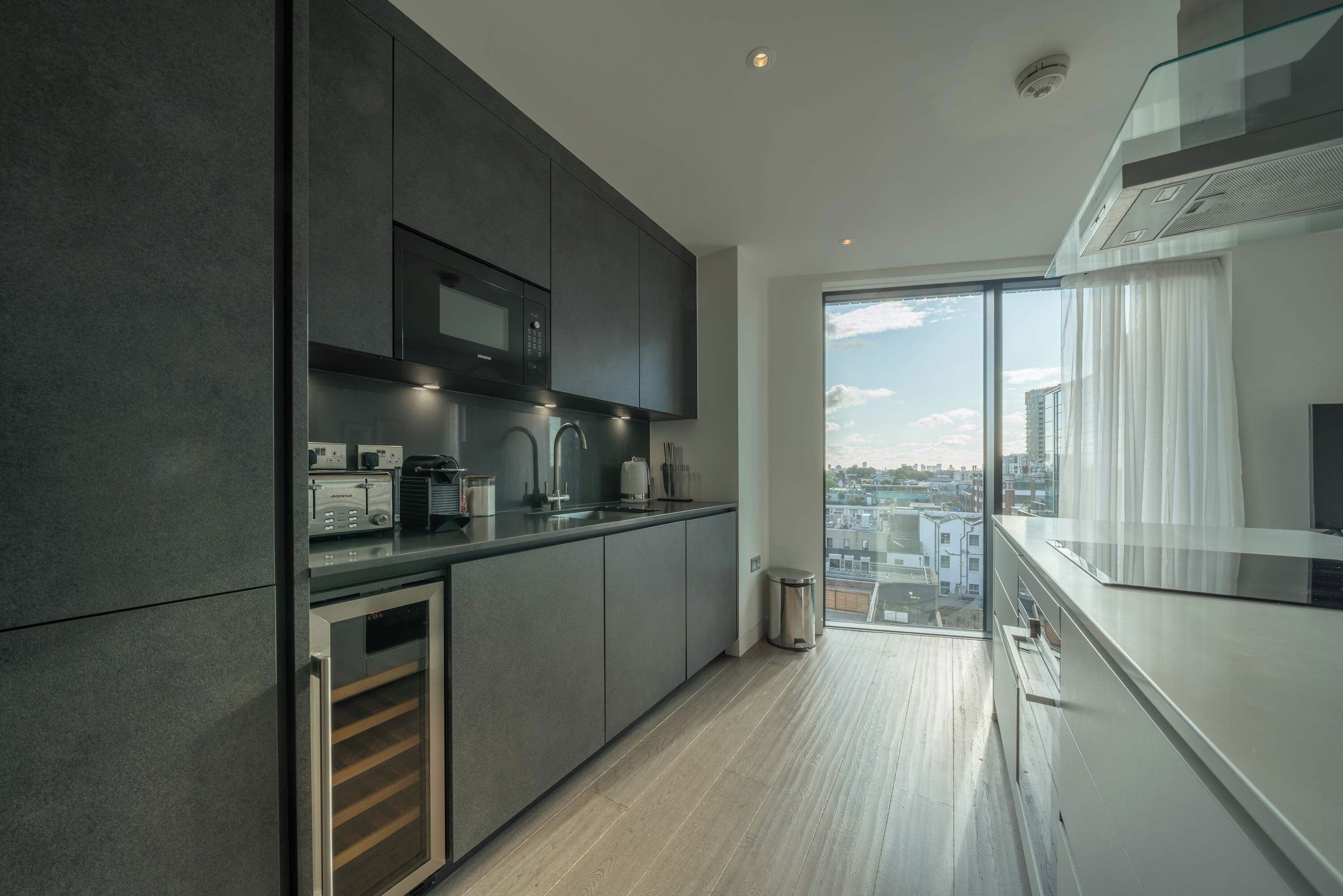 Une cuisine moderne dotée d’appareils électroménagers intégrés, d’une grande fenêtre et offrant une vue sur la ville.
