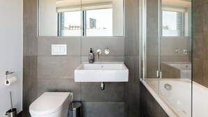 A modern bathroom with a toilet, sink, and bathtub. - Urban Minimalist Apartment with Private Balcony (Greater London)