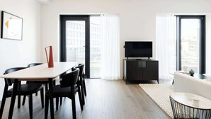 A modern living room with a dining area, a flat-screen TV, and large windows. - Urban Minimalist Apartment with Private Balcony (Greater London)