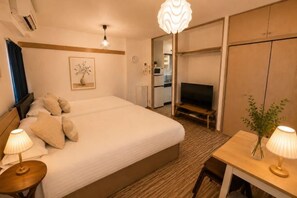 A hotel room with a large bed, a television, a desk with a lamp, and a wardrobe. - YMK Oshiage 6B (Tokyo)