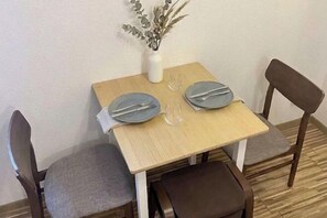 Een kleine eettafel met twee stoelen, een vaas met gedroogde planten en een paar brillen.