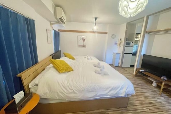 A hotel room with a bed, a TV, a bedside table, and a window with curtains.