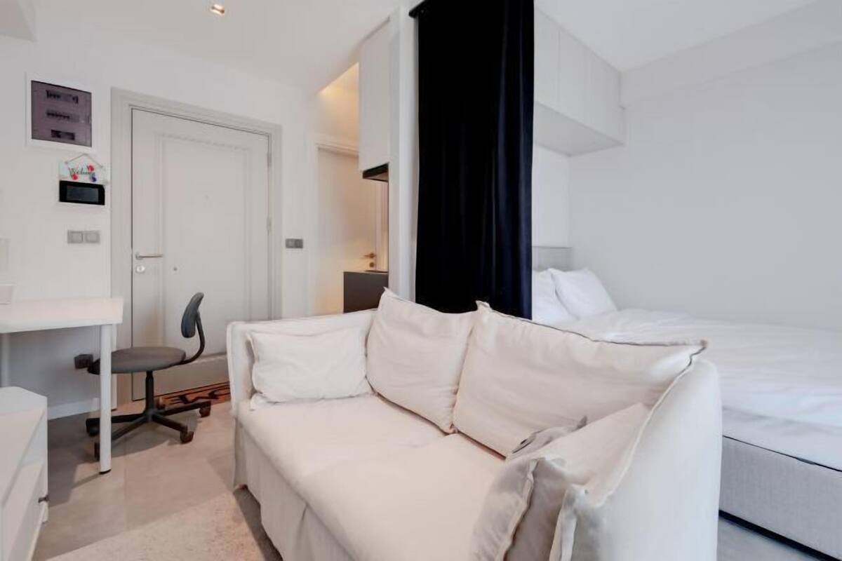 A hotel room with a white sofa, a desk with a chair, a bed, and a black curtain.