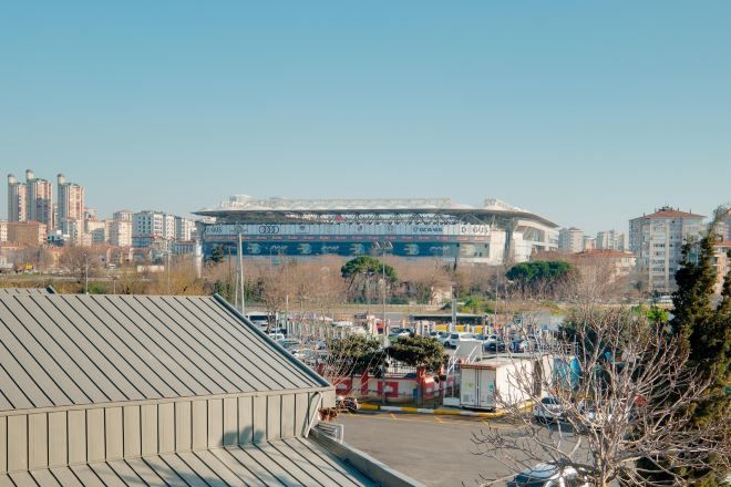 Um estádio com uma extensa área de arquibancadas e um estacionamento em primeiro plano.