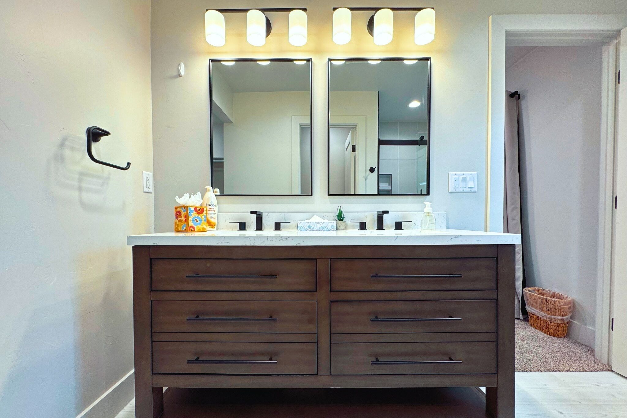 A bathroom with a double vanity, two mirrors, and overhead lighting.