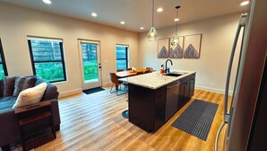 A modern kitchen with a central island, wooden flooring, and a dining area with a table and chairs.