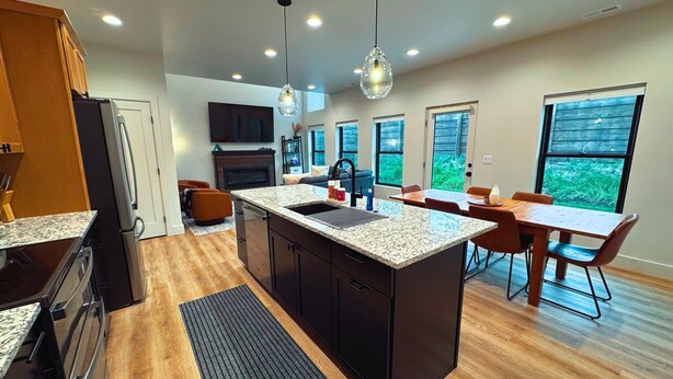 A modern kitchen with granite countertops, a central island, and a dining area with wooden tables and chairs.