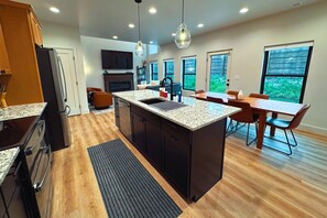 Une cuisine moderne dotée de plans de travail en granit, d’un îlot central et d’un coin repas avec des tables et des chaises en bois.