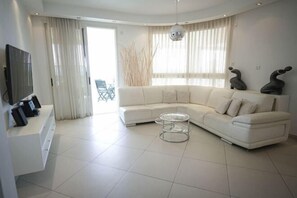 A modern living room with a white sofa, a glass coffee table, and a flat-screen TV on a white console.