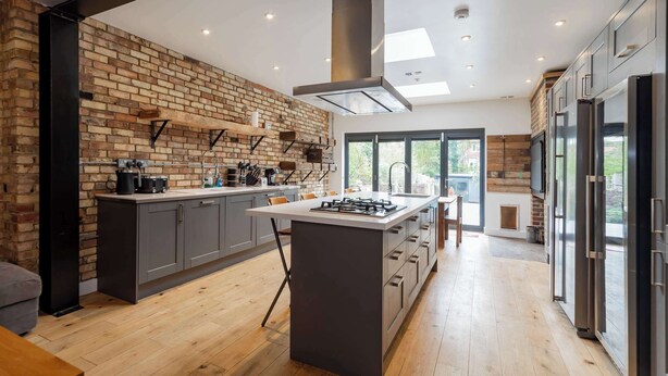 Une cuisine moderne avec un mur en briques, des meubles gris, un îlot central et des appareils électroménagers en acier inoxydable.