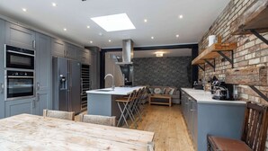 Une cuisine moderne avec des meubles gris, une table à manger en bois et un mur d’accent en briques.