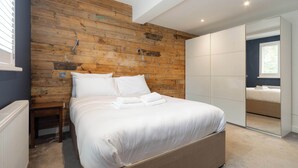 Une chambre avec un mur en bois, un lit recouvert de draps blancs, une petite table de chevet et une armoire à portes coulissantes.