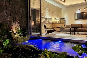 A modern interior with a stone wall, a glass door leading to a dining area, a blue-lit water feature, and a sofa. - K.House Phan Thiet by Blue Fingers (Phu Thuy)