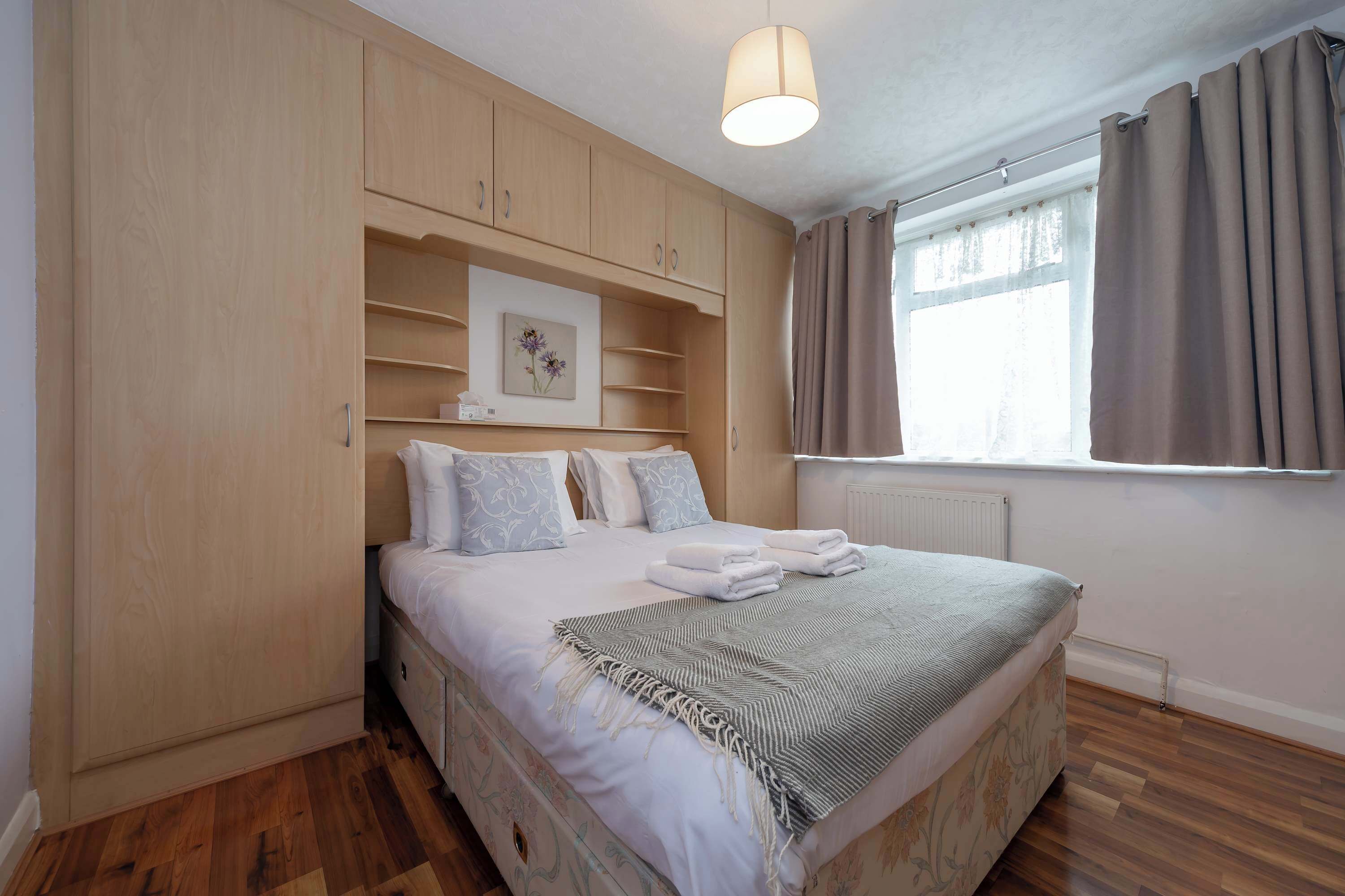 A bedroom with a bed, wooden wardrobe, a radiator, and a window with curtains.
