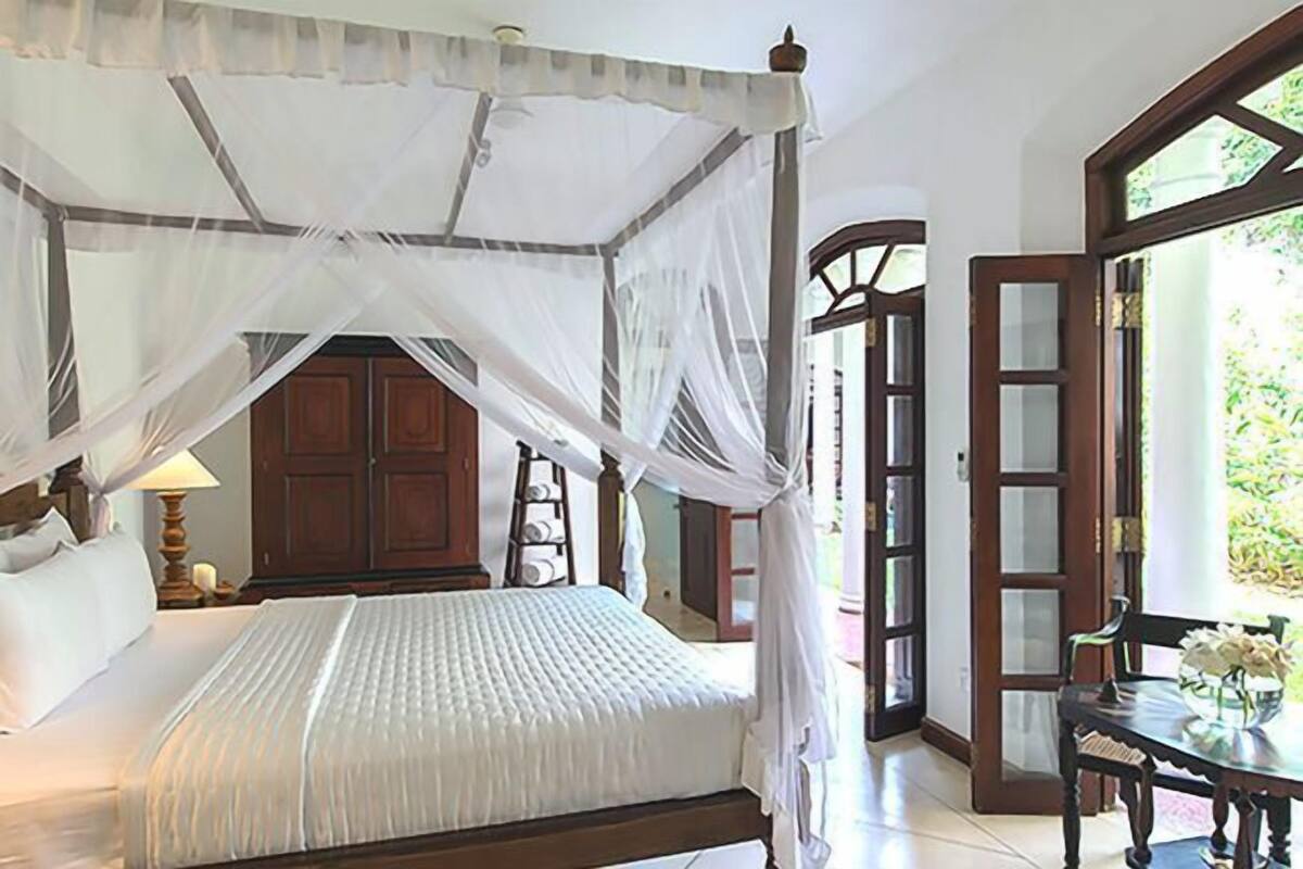 Een slaapkamer met een hemelbed, een houten garderobe en een groot raam.