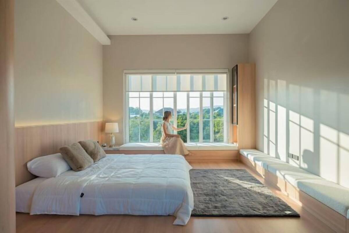 Ein Schlafzimmer mit einem großen Bett, einer Sitzbank am Fenster, einem Teppich und einem Nachttisch.