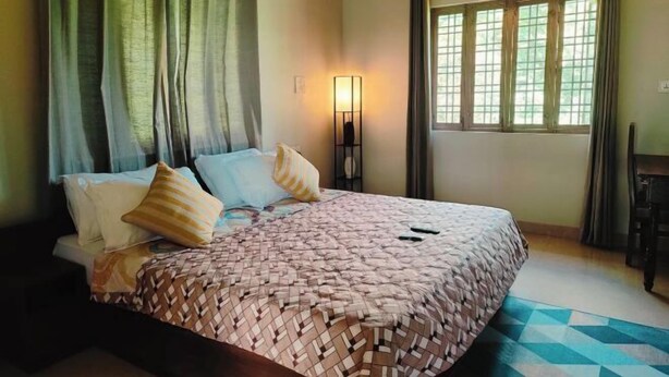 A bedroom with a bed, curtains, a wall-mounted lamp, and a window with curtains. - Hoztel Jollygrrant Doon (Dehradun)