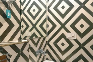 A bathroom with a geometric patterned wall, a mirror, a sink, and a towel rack. - Hoztel Jollygrrant Doon (Dehradun)