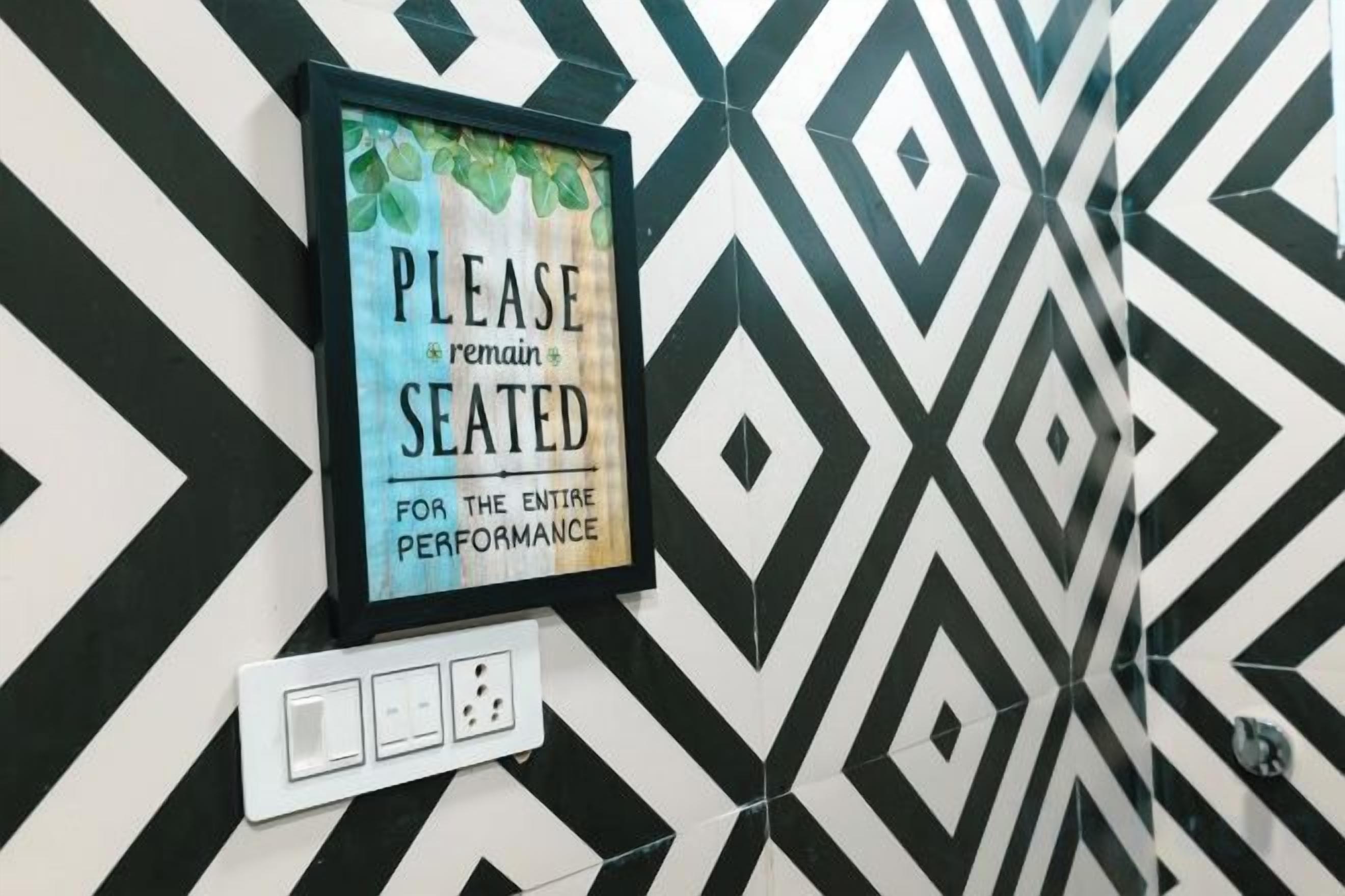 A framed sign on a wall with a geometric pattern, a power outlet, and a light switch.