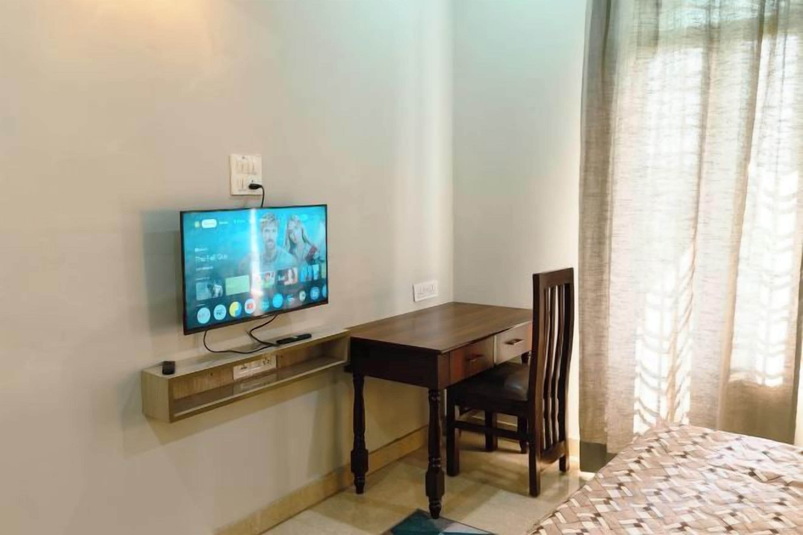 Une chambre dotée d’un téléviseur à écran plat fixé au mur, d’un bureau en bois avec une chaise et d’un lit recouvert d’une couvre-lit à motifs.