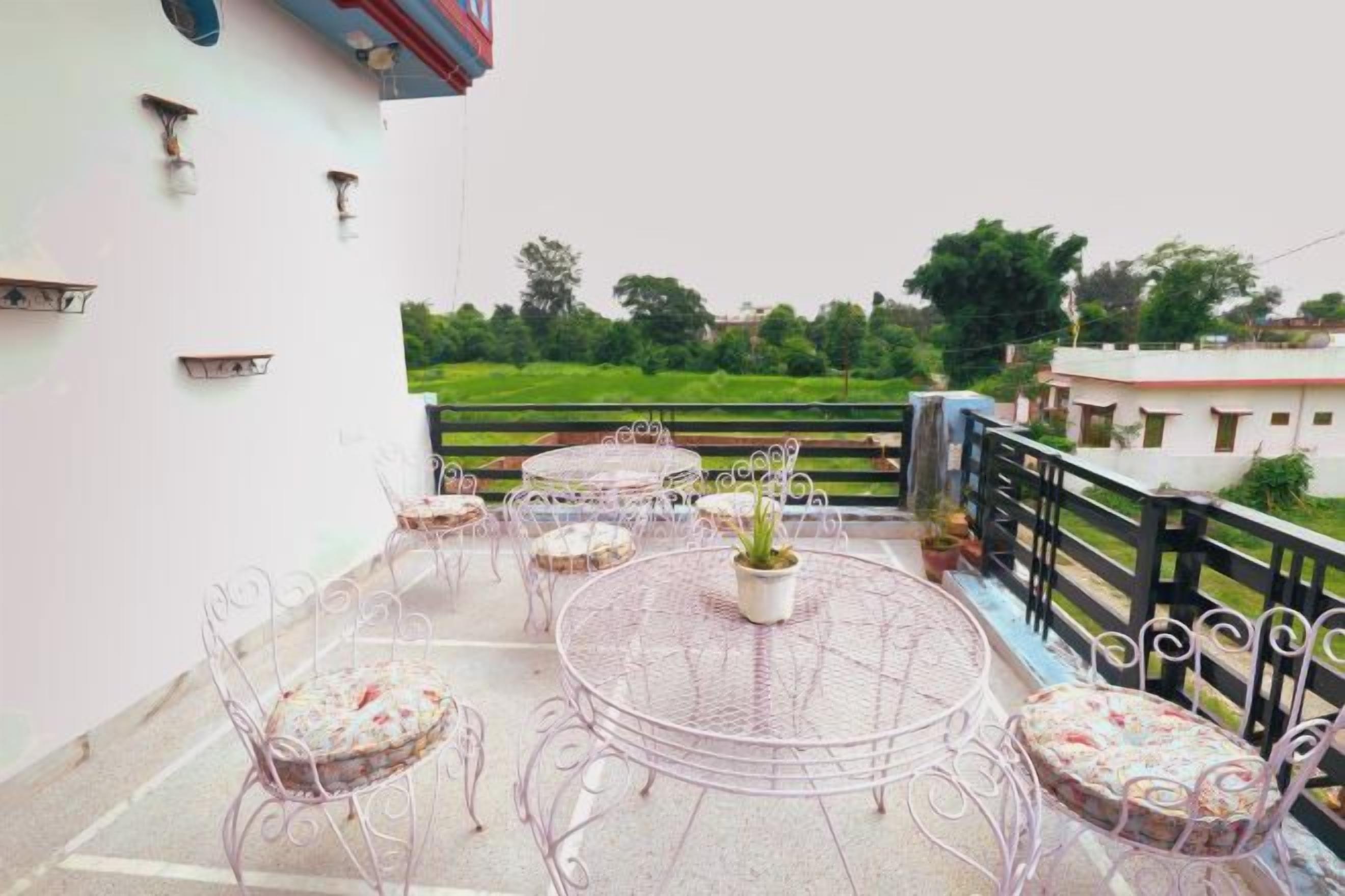 A balcony with a round table and chairs, a potted plant, and a view of a green landscape.