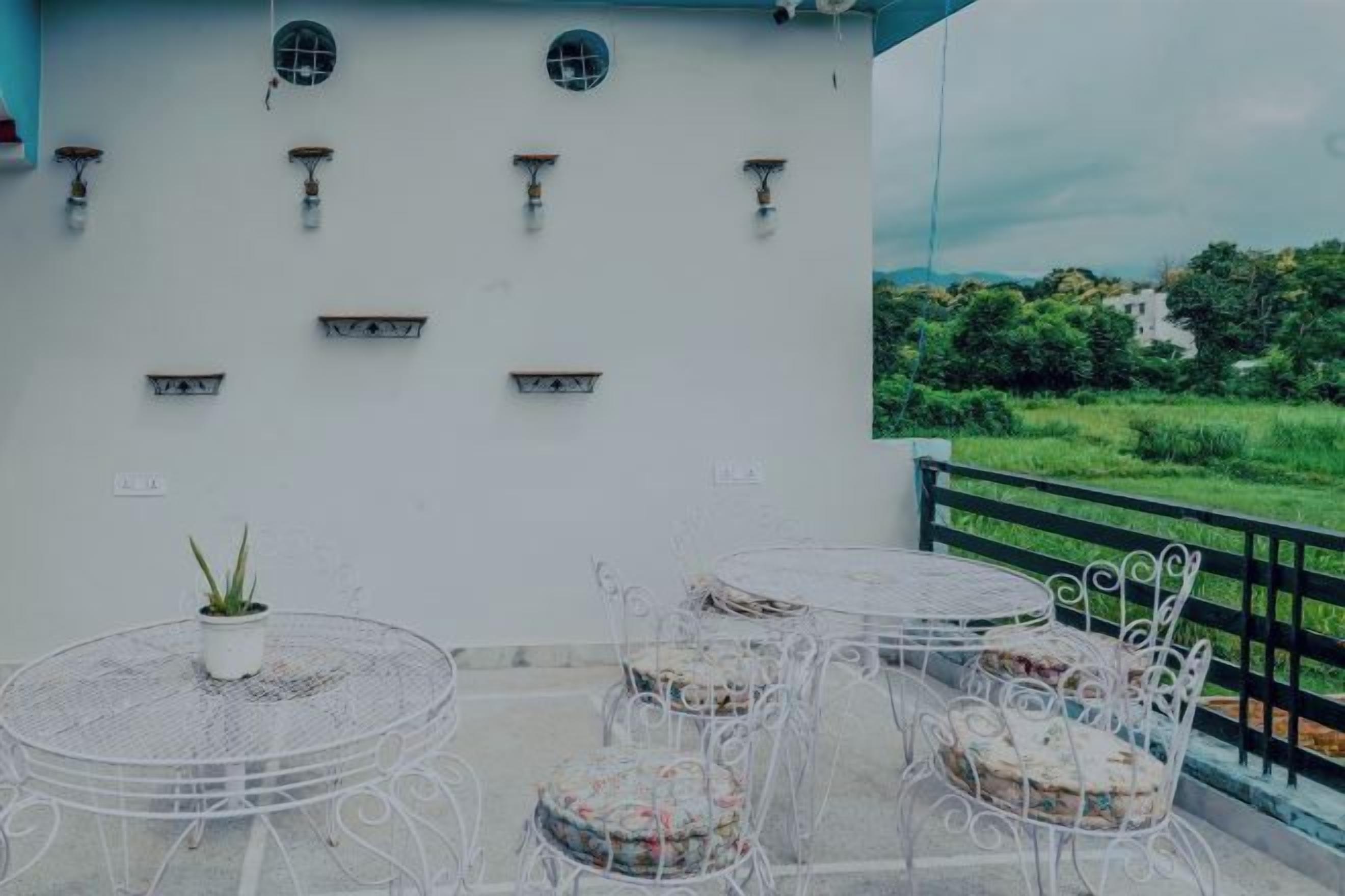 A balcony with outdoor seating, a white wall with decorative elements, and a view of greenery.