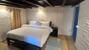 A bedroom with a bed, a nightstand, a wall-mounted lamp, and a blue door. - Beyond Wifi Burans Kot Heritage (Nainital)