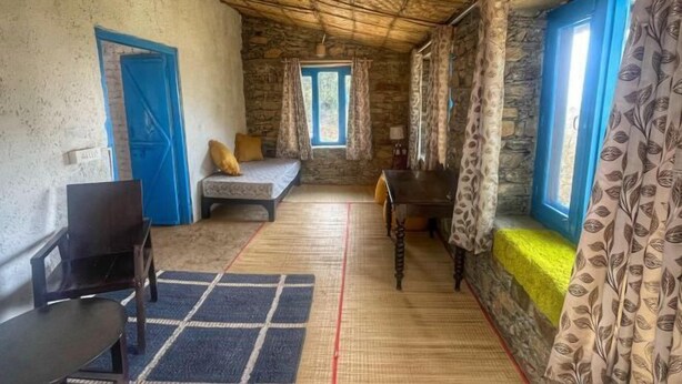 A rustic room with a stone wall, a wooden ceiling, a bed, a table, and a chair. - Beyond Wifi Burans Kot Heritage (Nainital)