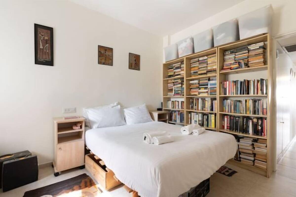 Een slaapkamer met een bed, een boekenkast, een nachtkastje en een koffer.
