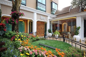 Un hotel boutique amb un jardí ben cuidat, una porta de fusta i un interior modern visible a través de la façana de vidre.